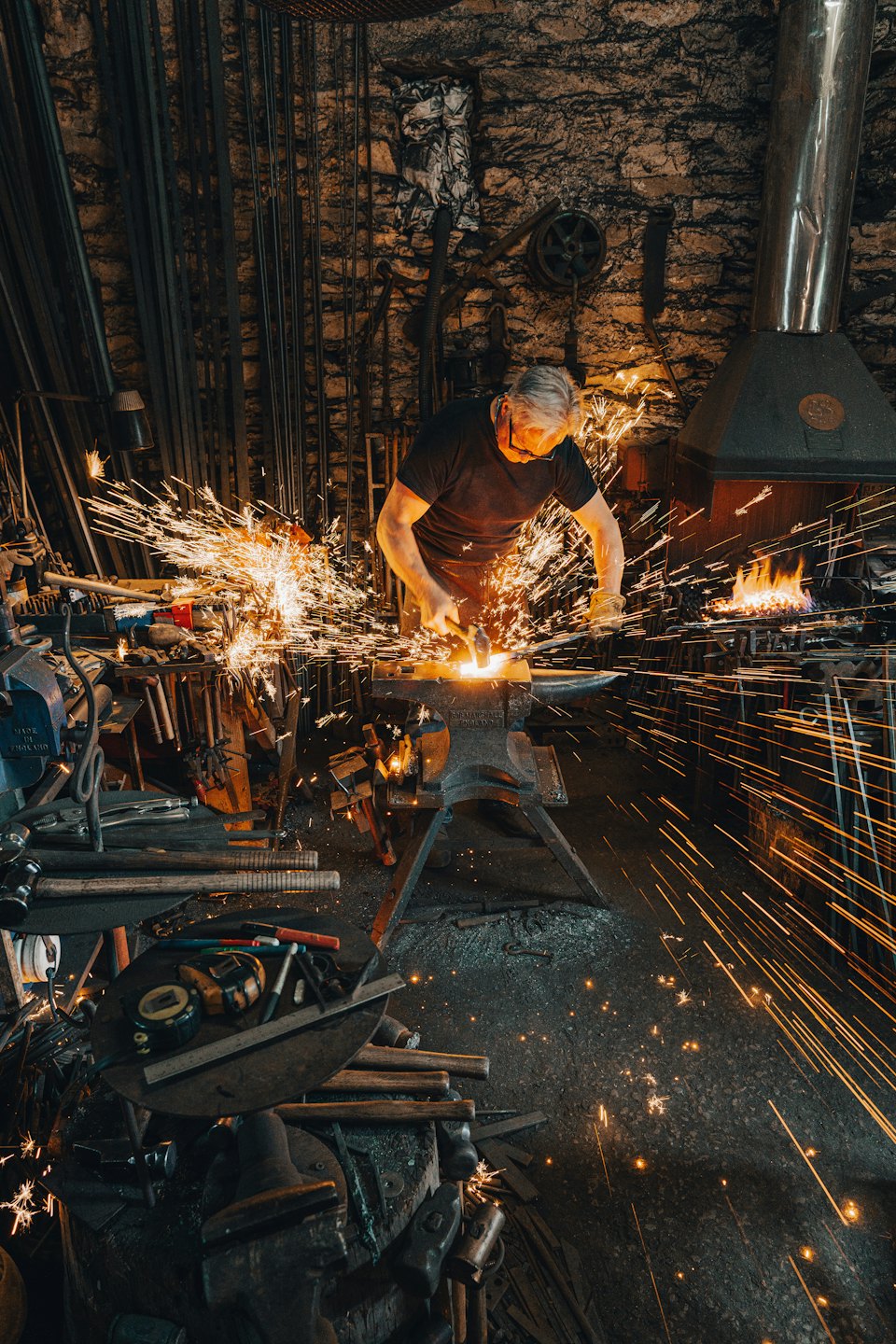 Blacksmith hammers glowing metal on an anvil.