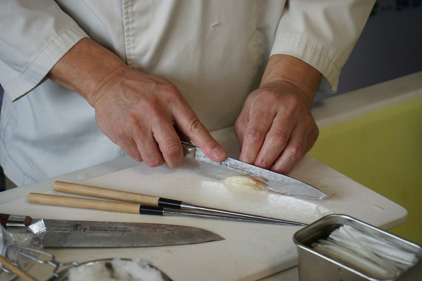 Chef slicing ingredient on cutting board in kitchen.