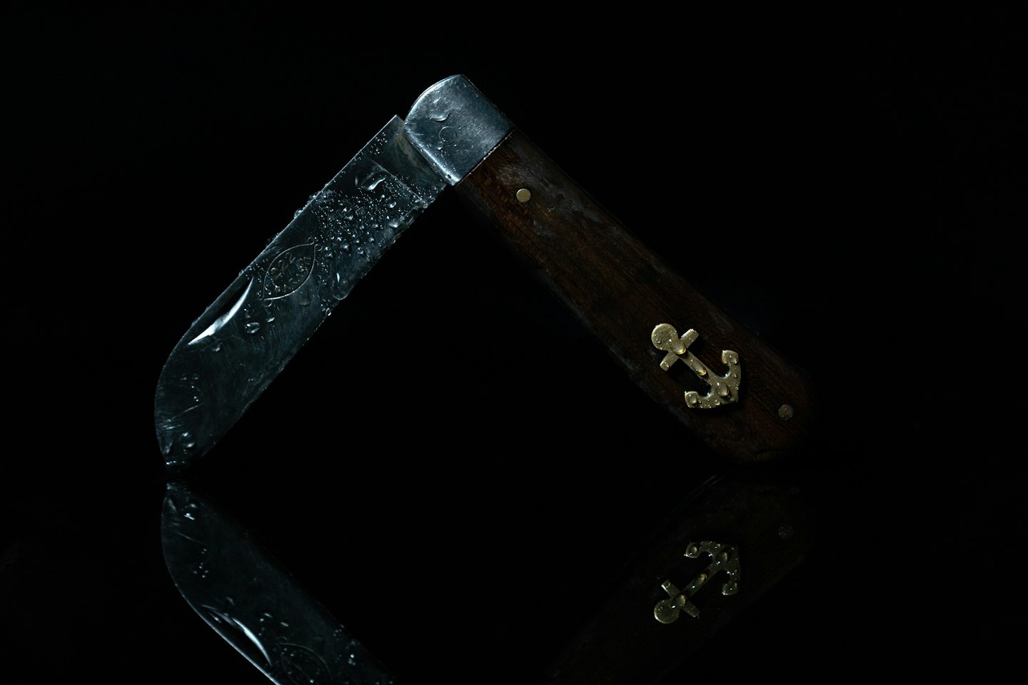 Folding knife with an anchor emblem sits on a surface.