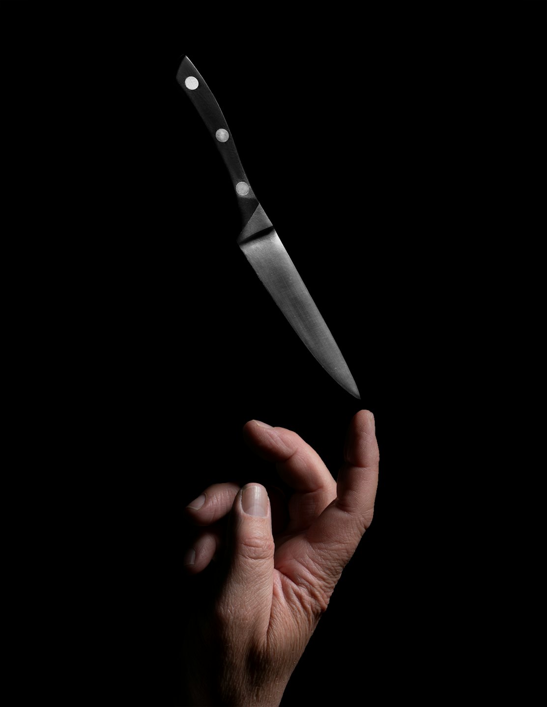 A hand balances a chef's knife upright on a finger.