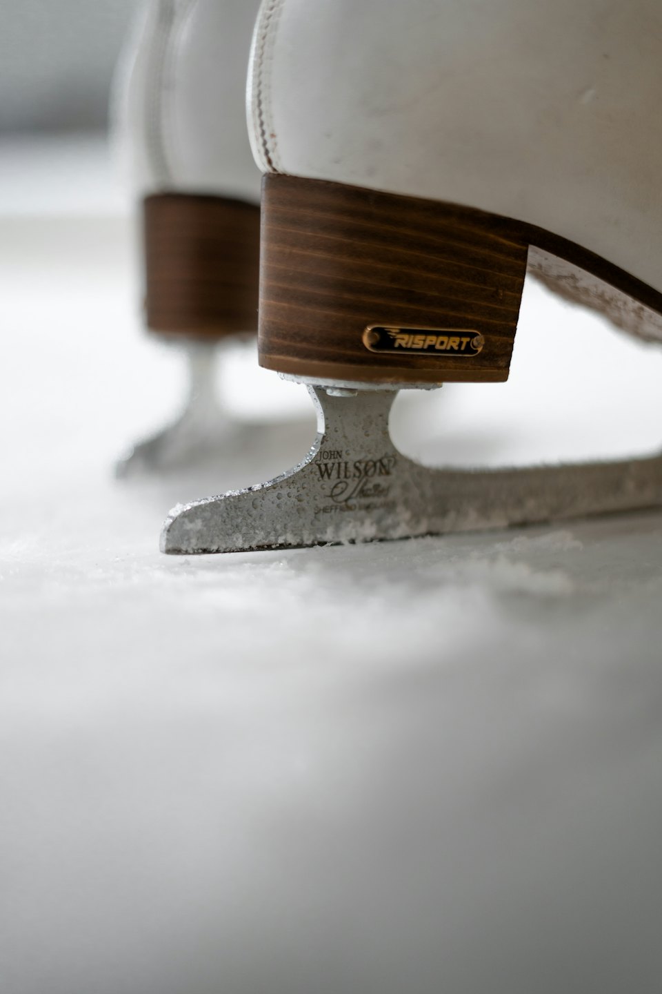 White ice skates with wooden heels on frosted ice.