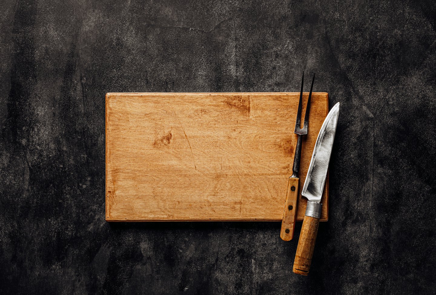 Chef's knife and carving fork on a wooden cutting board.